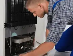 Refrigerator repair technician servicing the compressor and condenser area in Austin, TX