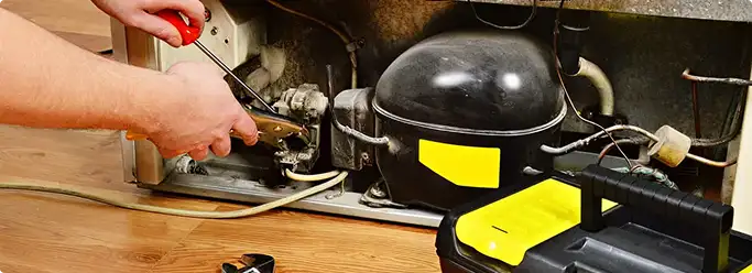 Refrigerator repair technician fixing the compressor and wiring in Austin, TX